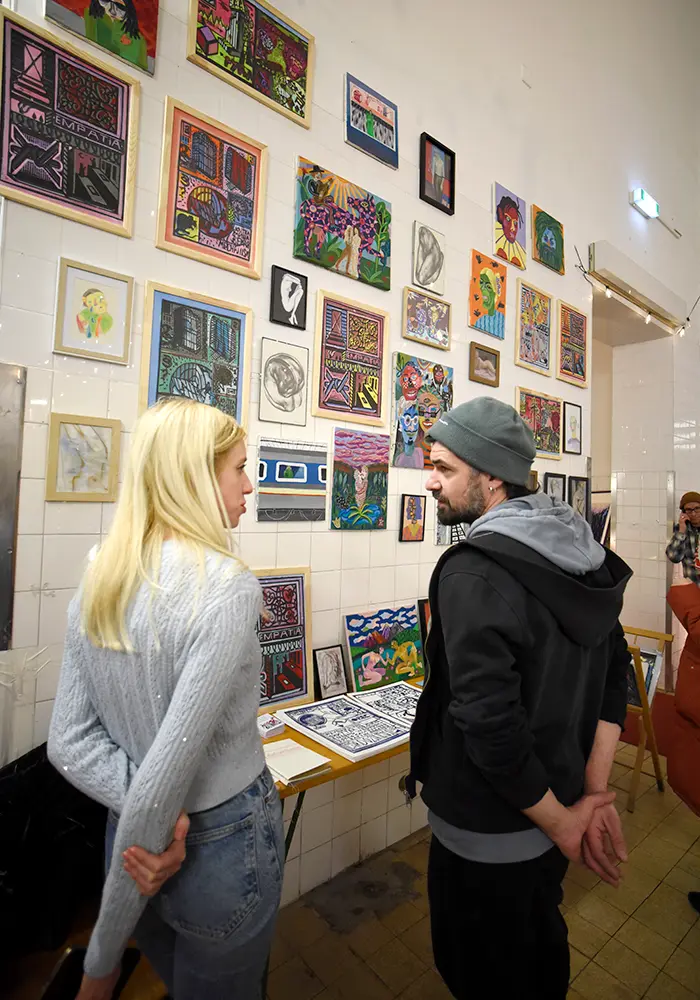 A man and a woman standing infront of a wall full of small paintings