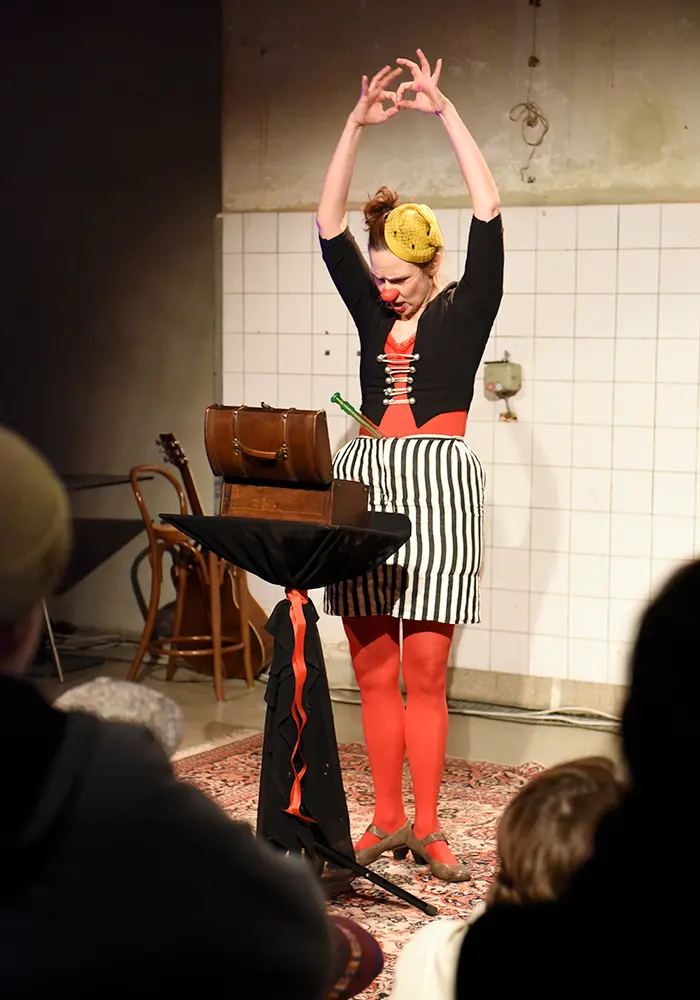 a clown artist is standing with raised hands infront of a small open wooden box